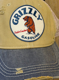 Thumbnail for A close-up of a distressed trucker hat featuring a tan front panel with a circular embroidered patch that reads 'Grizzly Gasoline' and shows a brown grizzly bear. The brim is made of faded blue denim with visible distressing and white contrast stitching, and the back is a light beige mesh.