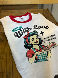 Thumbnail for A white ringer t-shirt with a red crew neck, featuring a retro-style graphic of a woman holding a pie and the text 'Made With Love AND SOME OTHER SHIT'. The shirt is laid flat on a rustic wooden table.