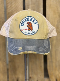 Thumbnail for A distressed trucker hat featuring a tan front panel and brim, beige mesh back, and a gray denim-look visor. The front has a circular embroidered patch with a grizzly bear and the text 'Grizzly Gasoline'.