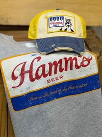 Thumbnail for A gray heather T-shirt with a large distressed vintage-style Hamms Beer logo print, styled with a matching yellow and navy blue trucker hat on top, 