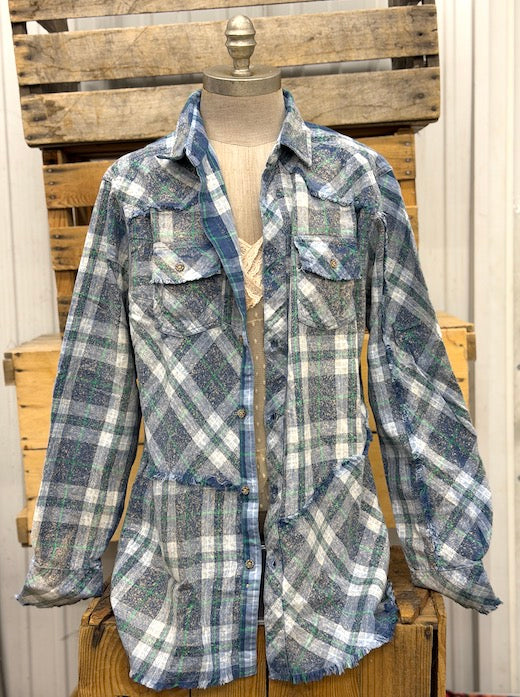 A long-sleeve plaid button-up shirt jacket in blue, gray, and white, displayed on a dress form mannequin against a rustic wooden crate backdrop.