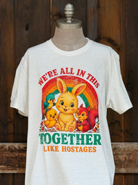 Thumbnail for A white graphic t-shirt The graphic features a distressed retro design with a yellow bunny, a red squirrel, a yellow duckling, and a rainbow, with the text 'WE'RE ALL IN THIS TOGETHER LIKE HOSTAGES'.