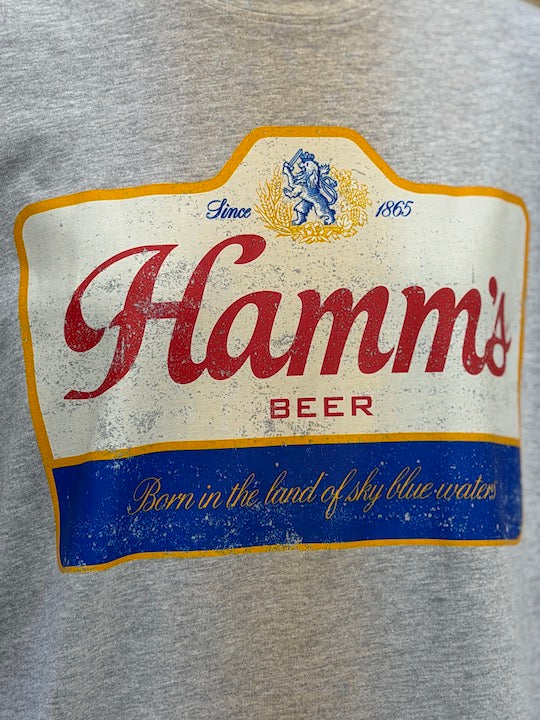 Close-up of a heather gray sweatshirt featuring a distressed vintage-style print of the Hamm's Beer logo with red lettering, a blue banner, and gold accents.